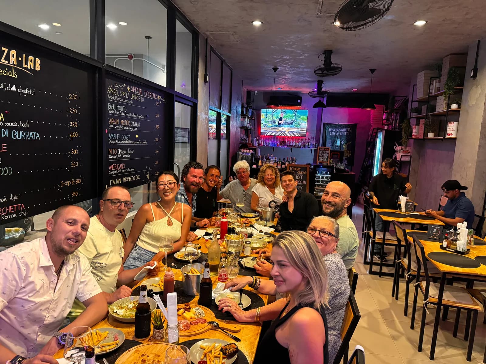 A big group of guests smiling around a long table at Pizza Lab at night