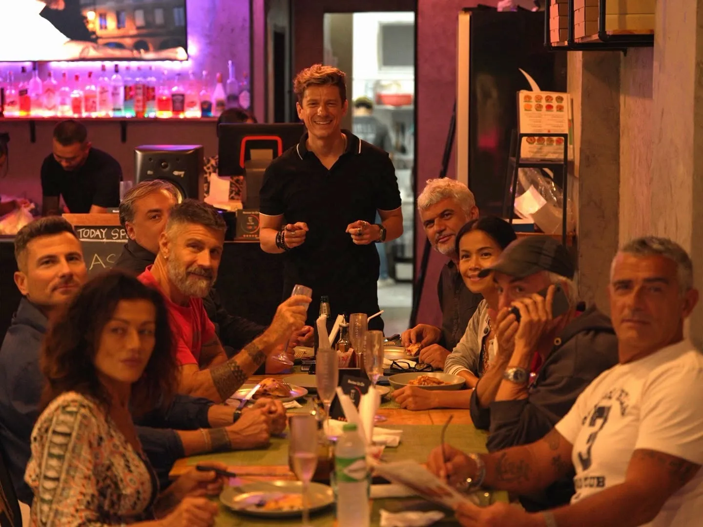 A group of friends at a long table at Pizza Lab, with the host smiling behind them