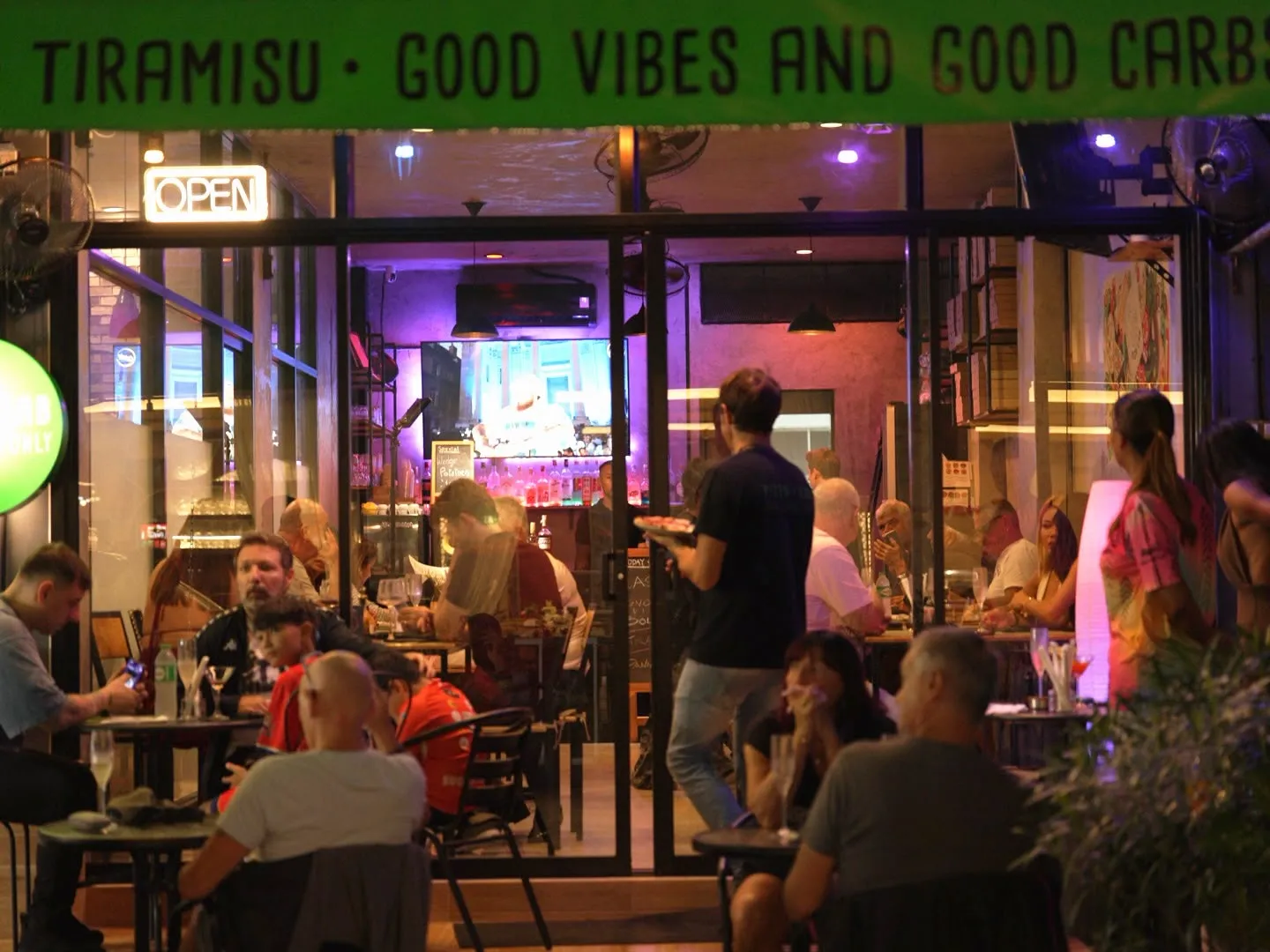 Pizza Lab Patong at night: guests on the terrace, a lit OPEN sign and the busy dining room behind the glass